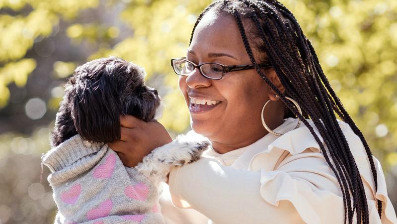 迈拉·布朗在户外公园抱着她的狗。迈拉接受了一次成功的手术，从她的胰腺上切除了一个肿块。