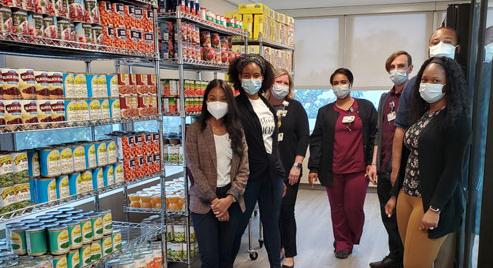 A team of MedStar Health associates wearing masks standing next to shelves of food inside a food distribution center.