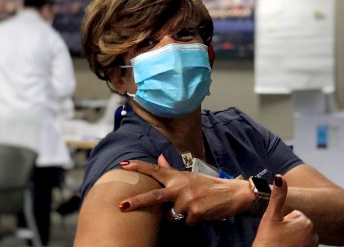 戴口罩的护士在接受COVID疫苗注射后竖起大拇指