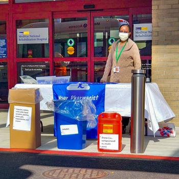 Two MedStar pharmacists wearing masks work at an event to take back unused drugs and pharmaceutical paraphenalia for safe disposal.