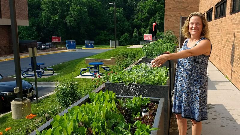 A MedStar Health associate waters a garden in front of a hospital building.