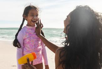 A smiling little surfer girl who is having her mother put sunscreen lotion on her nose.