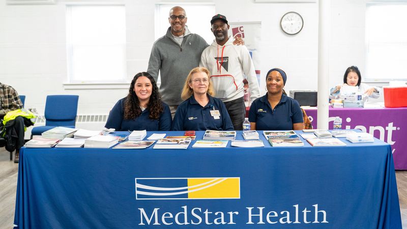 A group of MedStar Health associates pose for a photo behind a presentation table at a community health event.