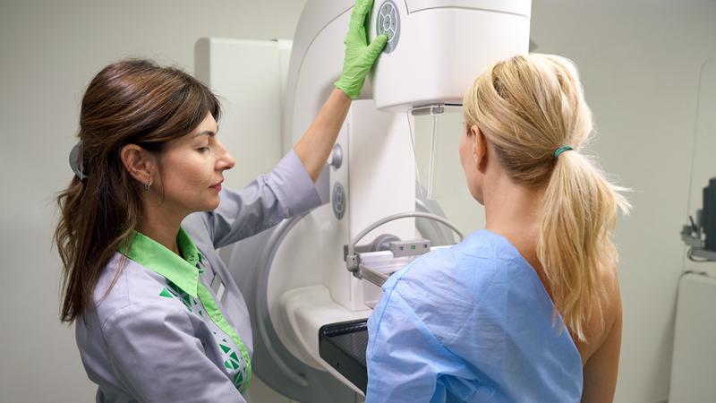 A mammography technician positions a patient for a mammogram scan in a clinical setting.