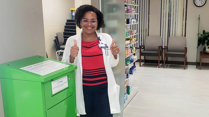 A pharmacist gives the thumbs up as she stands next to a drug disposal receptacle at MedStar Health.