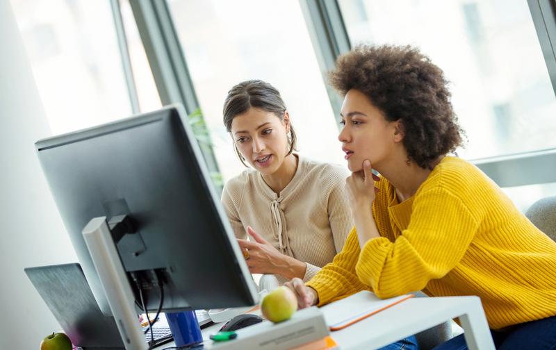 Two women work at a computer in an office.