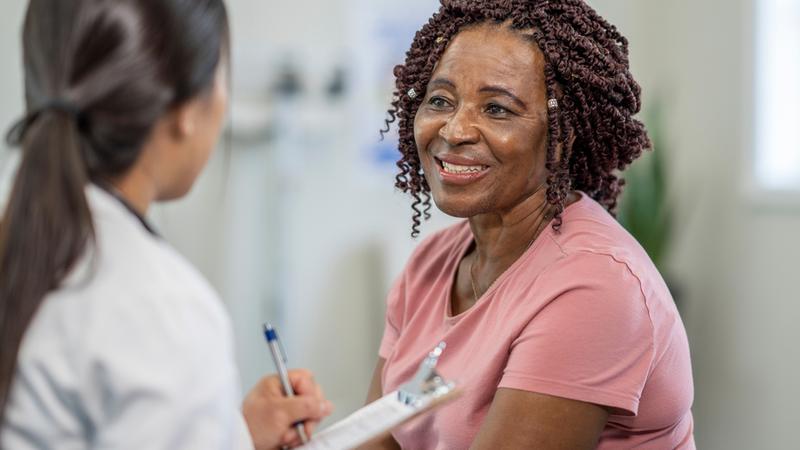 A female african american patient smiles while talking with her doctor in a clinical setting.