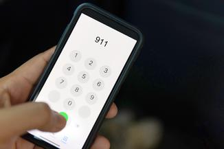 Photo of a hand holding a cell phone about to dial 911.