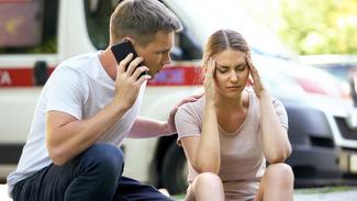 A young man calls for help while helping a woman who was injured in a car accident.