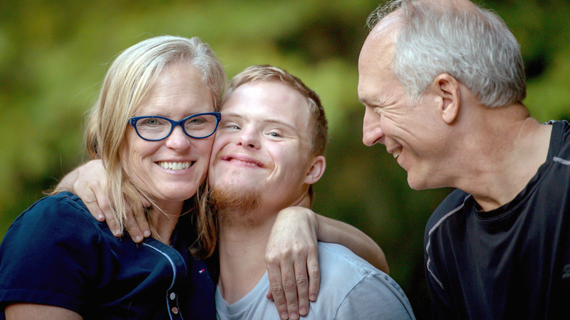 A mom puts her arm around her young adult son's shoulder while the father smiles.