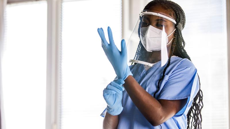 A medical professional puts on gloves and PPE.