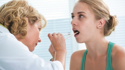 A doctor uses a tongue depressor to look in a patient's mouth.