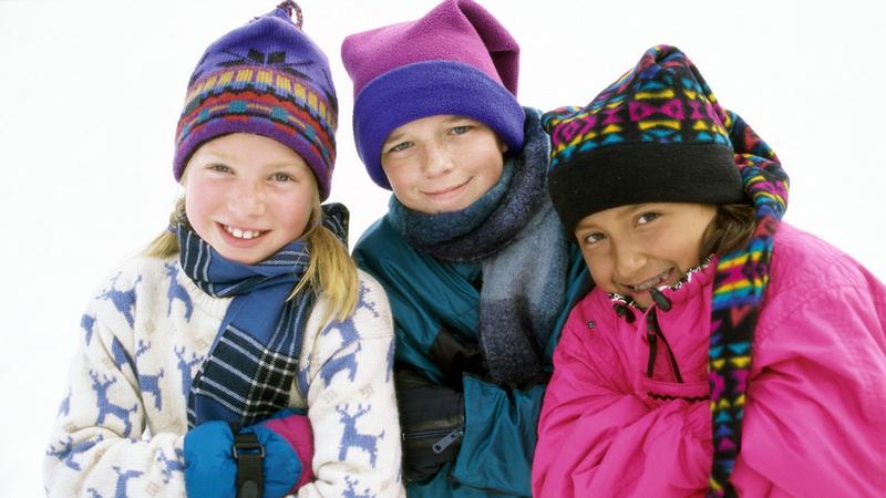 Three children dressed in hats and coats stand in the snow.