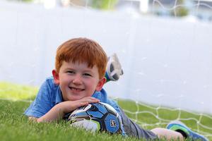 A young boy lays in the grass outdoors.