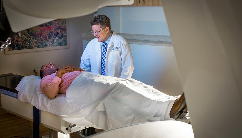 Dr Sean Collins talks with a patient who is laying on the bed of the cyberknife at MedStar Georgetown University Hospital.