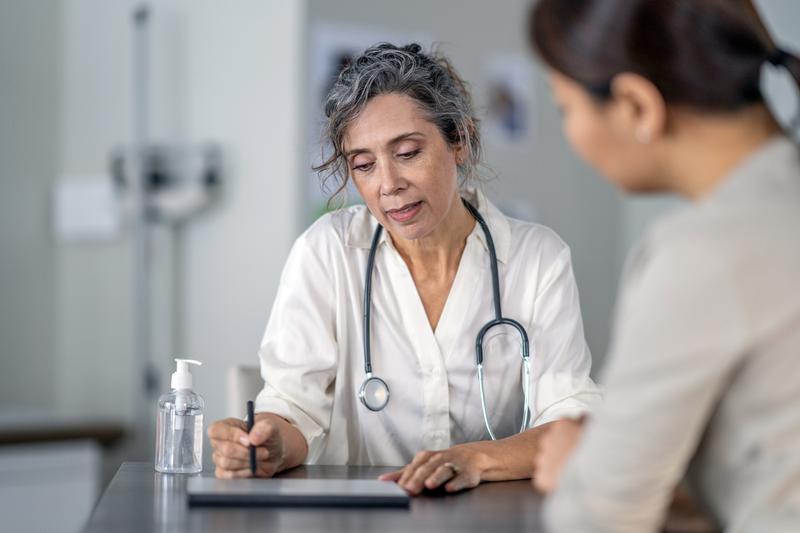 A doctor talks to a patient sitting at a table in an office.