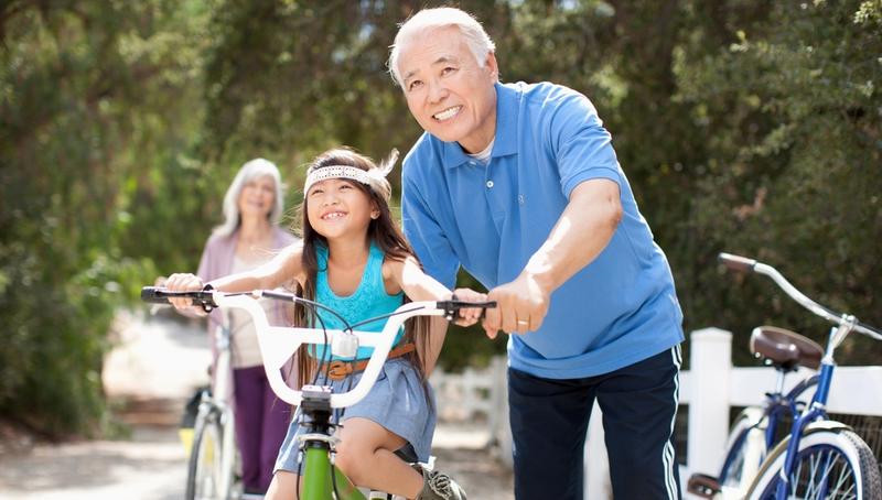 A grandfather helps his granddaughter learn to ride a bike.