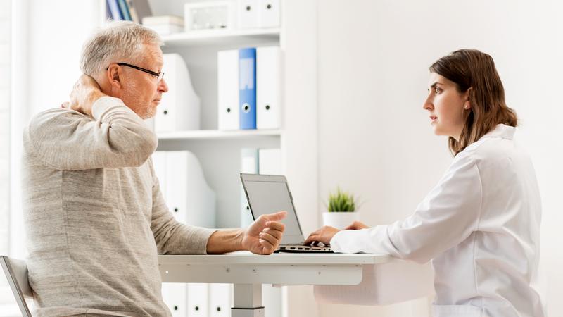 A senior man holds his neck as he consults with his doctor in a clinical setting.