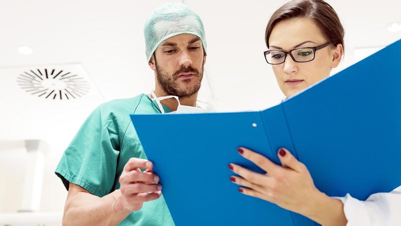 Two doctors look at a binder of papers.