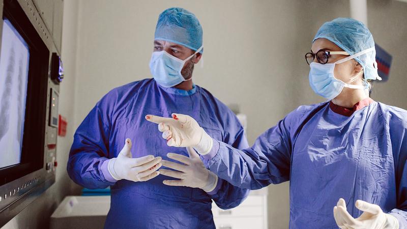 Two surgeons consult in front of a light box in a clinical setting.