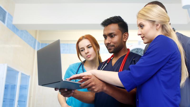 Healthcare professionals look at a laptop computer in a hospital setting.