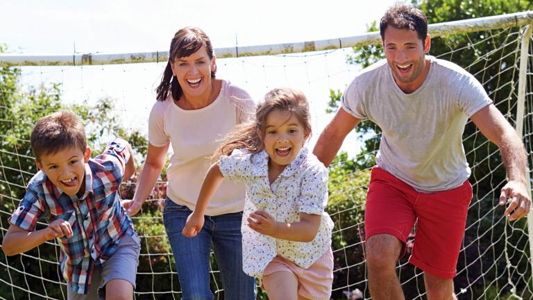 A family play soccer together outdoors.