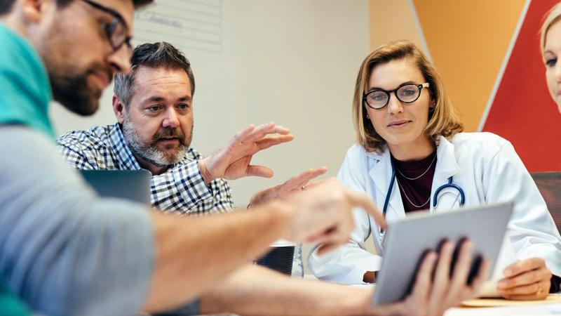 A group of doctors talk while looking at an ipad.