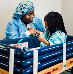 A dentist wearing blue scrubs and a blue hair covering, poses with a young girl patient.