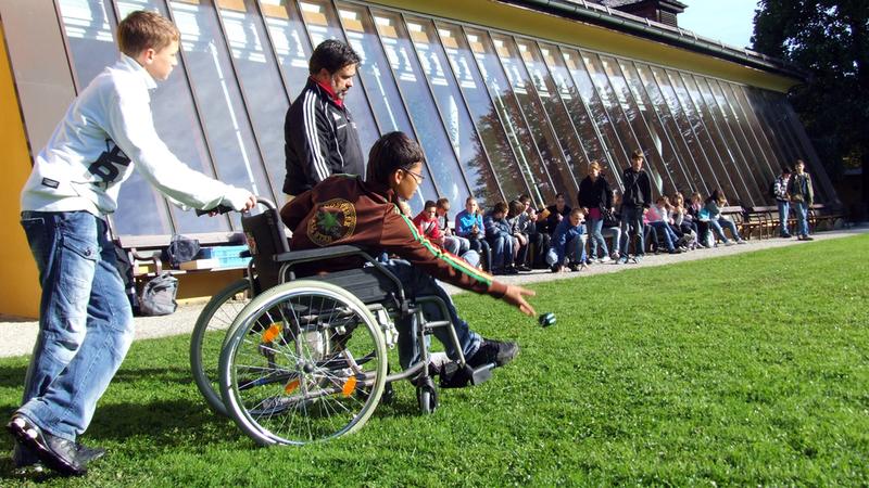 A young boy in a wheelchair plays a game outdoors.