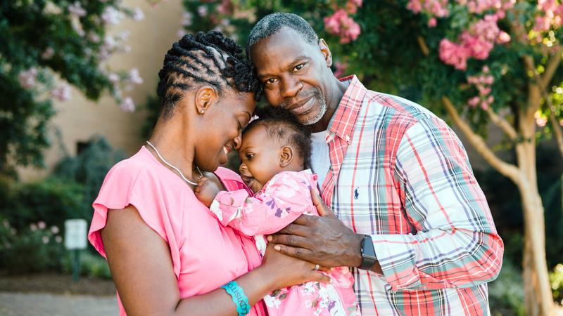 A mother and father hold their young child outdoors.