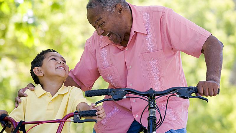 A senior man bicycles with his grandson.