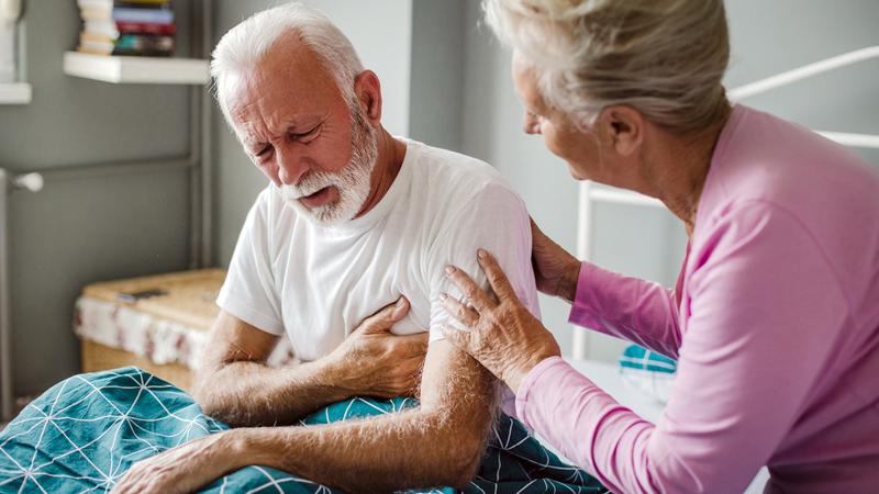 A senior woman helps her husband while he is experiencing chest pain at home.