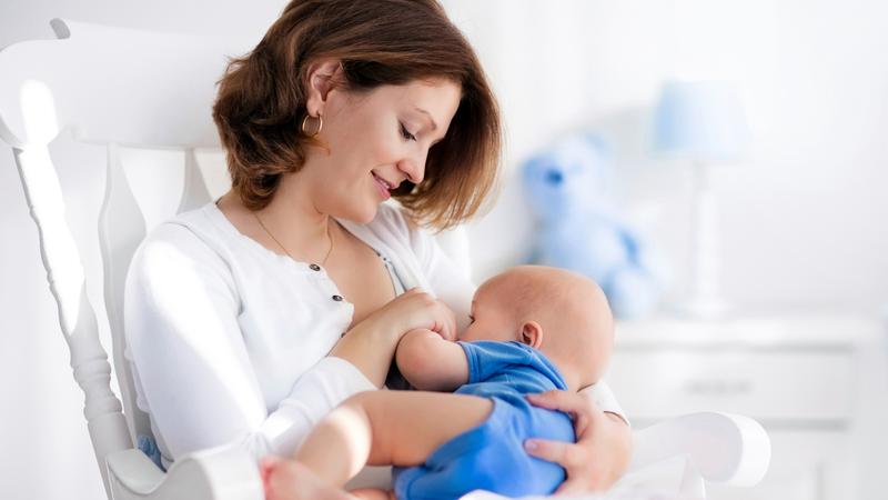 A mother breastfeeds her baby at home.