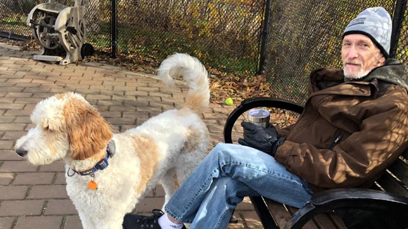 Ed Gershkovich sits with his dog in a park outdoors in cold weather.