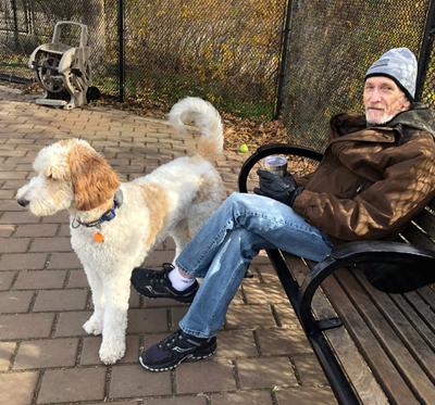Ed Gershkovich sits with his dog in a park outdoors in cold weather.