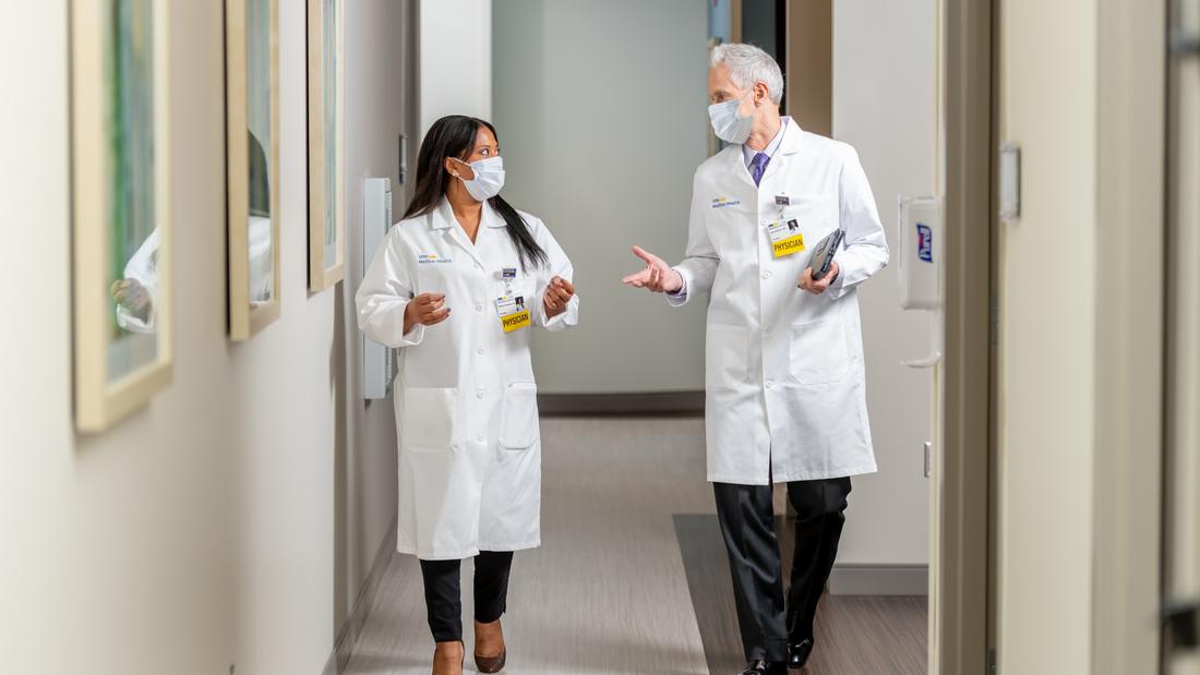两名戴着口罩的医生一边交谈，一边走在医院的走廊上。