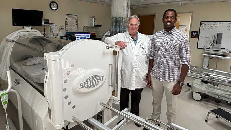 Dr. Richard Greengold and his patient Mouhamed Niang stand next to a hyperbraric oxygen therapy machine at MedStar Health.