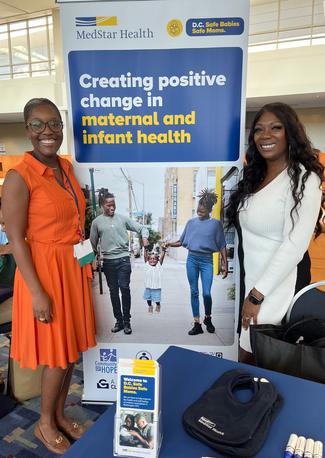 Roxane Richardson and Jodi Ann Boreman stand together at a conference next to a banner for the Safe Babies Safe Moms program.