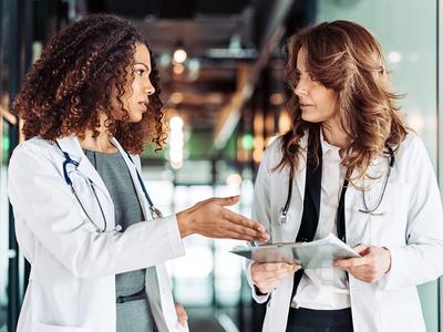 Two female doctors talk as the walk down a hallway.