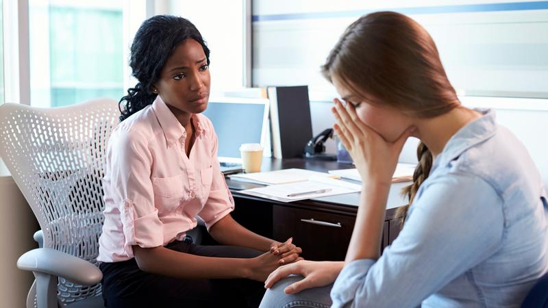 A woman cries while talking to a behavioral health professional in a clinical setting.