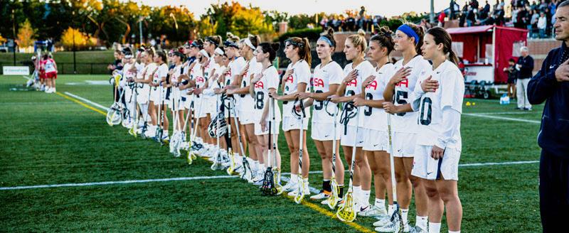 A USA Lacrosse team stands in a line along the sideline with their hands over their hearts during the playing of the national anthem, prior to the start of a game.