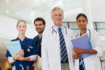 A group of medical professionals, shot from a low angle, stands in a lobby and poses for the camera.