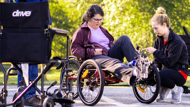 A MedStar Health professional helps fit a woman in an adaptive fitness recombent bike.