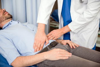 A doctor in white coat palpating belly of man lying on exam table.