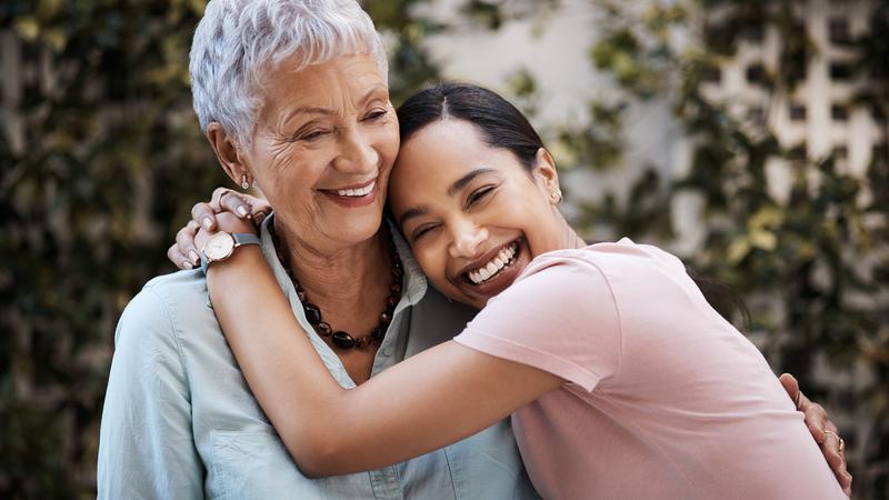 a young woman lovingly hugs a senior woman in an outdoor setting.