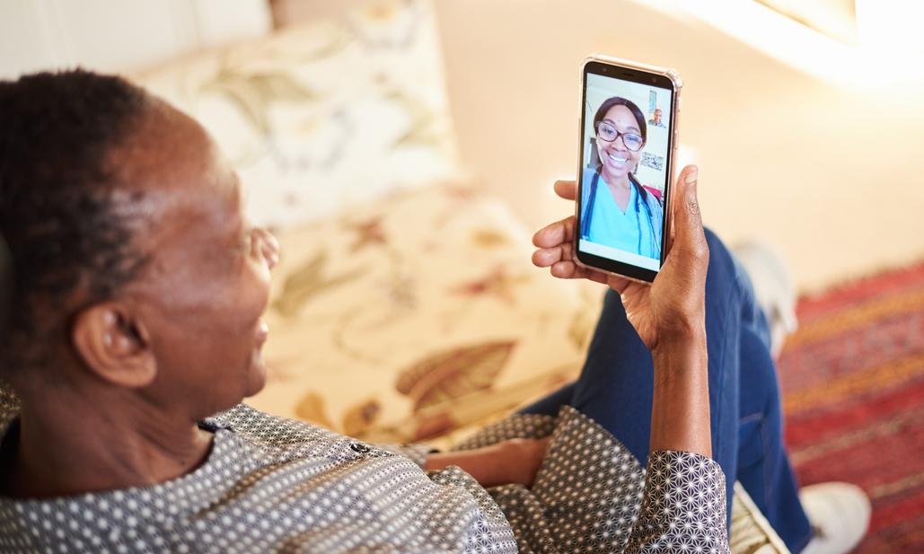 Senior African American woman using a smart phone app to consult with a doctor in real time while sitting at home
