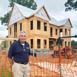 Craig Ruppert from Rupert Landscaping, wearing a blue polo shirt, looks at the camera as he stands in front of a house under construction.