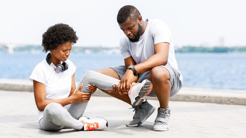 A man crouches down to look at the ankle of a young woman who is injured.