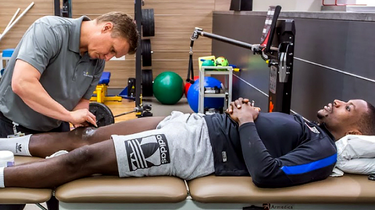 An athletic trainer examines the knee of an athlete so that he can achieve his personal goals.