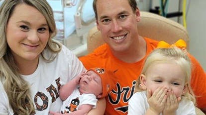 A family wearing Baltimore Orioles' shirts holds their newborn baby